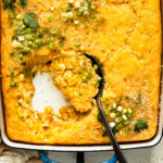 Overhead photo of creamed corn casserole in a blue baking dish with a serving spoon inserted into casserole.