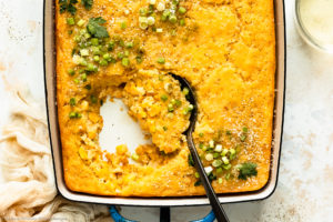Overhead photo of creamed corn casserole in a blue baking dish with a serving spoon inserted into casserole.