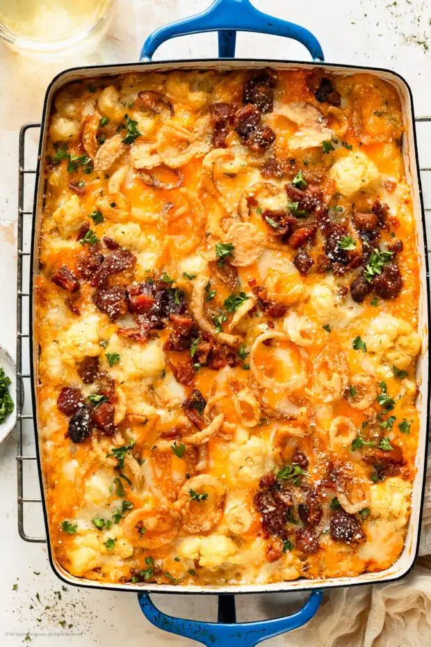 Overhead photo of a loaded cauliflower bake topped with crispy bacon and shredded cheese.