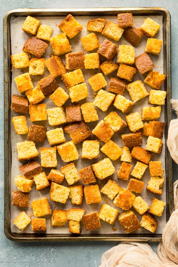 Overhead photo of toasted cubes of cornbread on a baking sheet.