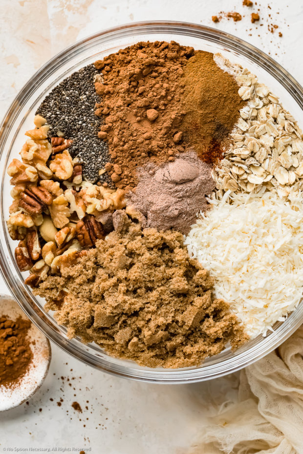 Overhead photo of the all ingredients in the chocolate granola recipe neatly arranged in a large mixing bowl before being mixed together. to make chocolate granola