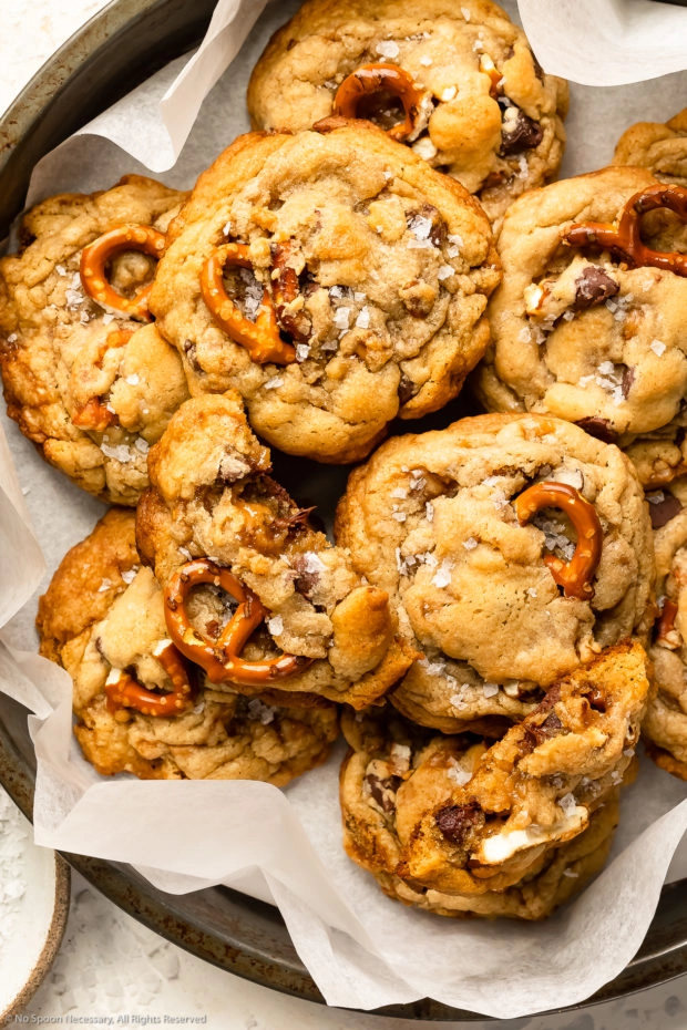 Overhead photo of a bunch of kitchen sink cookies piled into a parchment paper-lined pan - with one cookie broken in half.