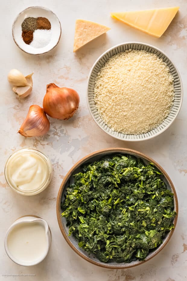 Overhead photo of the eight ingredients needed to make baked creamed spinach recipe neatly organized on a kitchen counter.