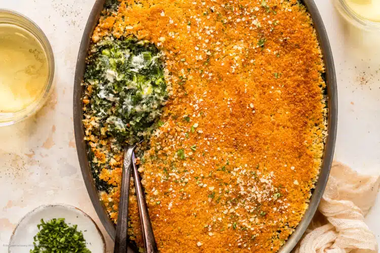 Overhead photo of baked creamed spinach in a casserole dish with two serving spoons inserted into the spinach.