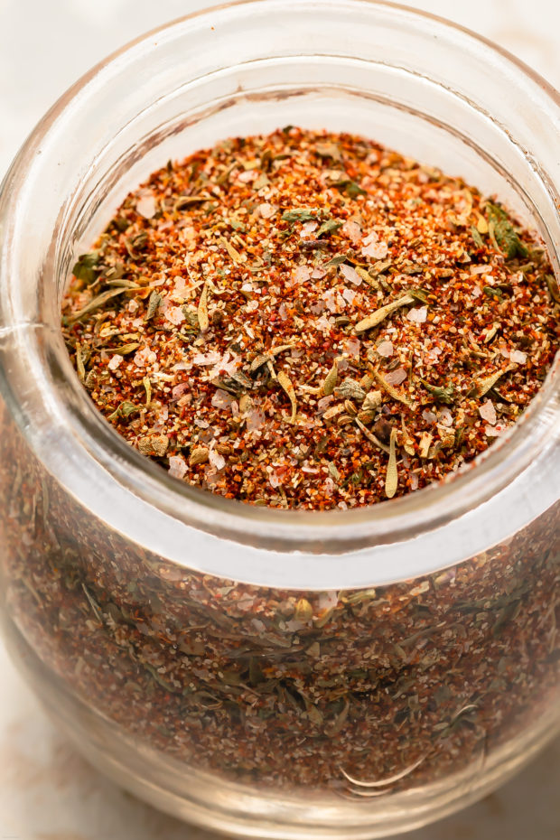 Close-up, angled photo of Cajun spice blend in a small glass jar.