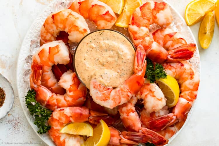 Overhead photo of a platter of shrimp cocktail and lemon wedges with a bowl of remoulade sauce in the middle of the platter.
