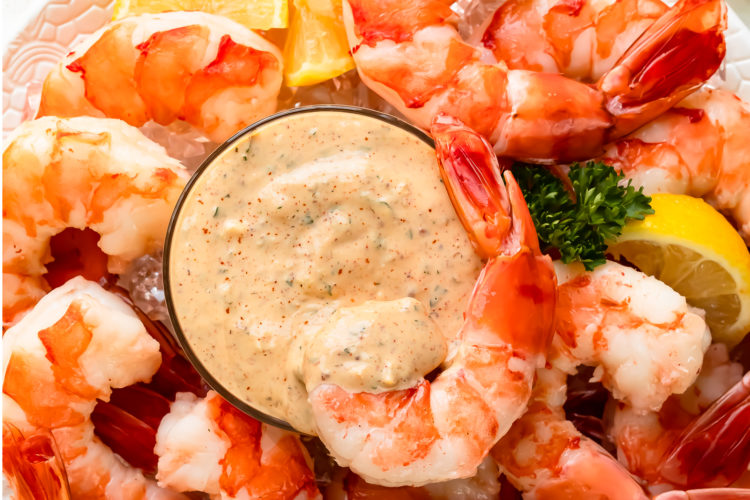Overhead photo of a platter of shrimp cocktail and lemon wedges with a bowl of remoulade sauce in the middle of the platter.