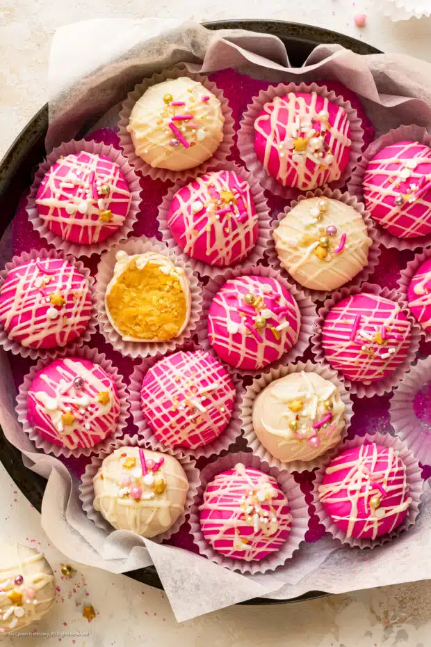 Overhead photo of pink and white cake bites in a paper-lined metal tin. 