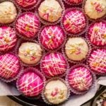 Overhead photo of hot pink and white homemade cake bites in a cookie tin with a bowl of sprinkles next to the tin.