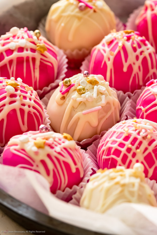 Angled, close-up photo of a white cake bite truffle decorated with gold, pink and white sprinkles