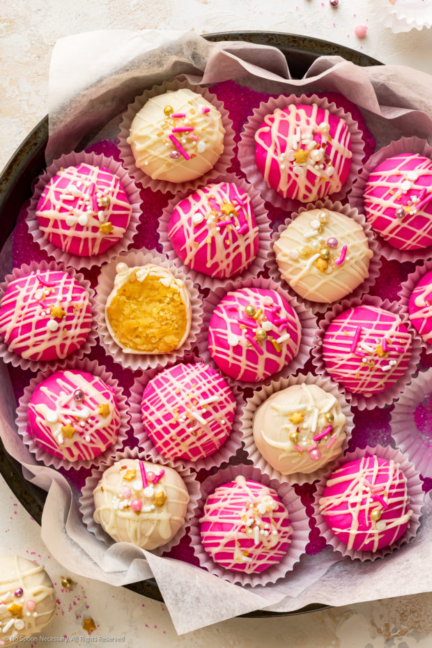 Overhead photo of pink and white cake bites in a tissue paper-lined metal tin. 