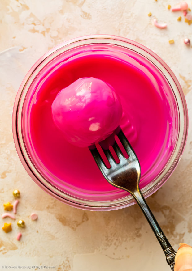 Overhead photo of a cake ball being dipped into hot pink melted candy.