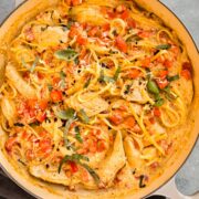 Overhead photo of chicken pasta with tomatoes, basil, and cheese in a large skillet.
