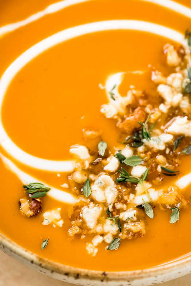 Angled, close-up photo of cream of sweet potato soup garnished with crumbles of cheese, fresh herbs and crunchy walnuts.