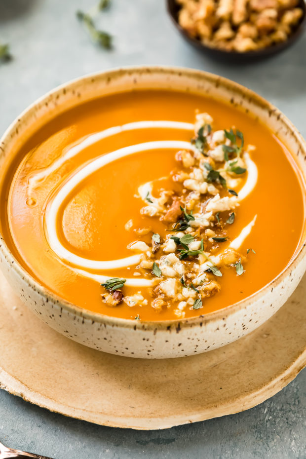 Angled photo of sweet potato bisque topped with fresh herbs and walnuts in a beige soup bowl.