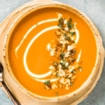 Overhead photo of Sweet Potato Soup topped with fresh herbs in a beige soup bowl.