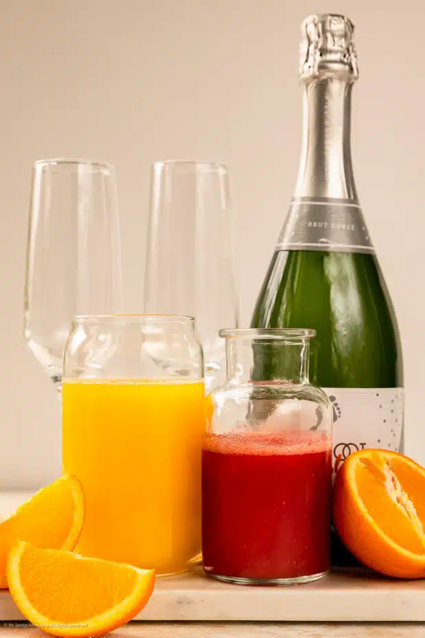 Straight on photo of champagne, orange juice, and strawberry puree for mimosas.