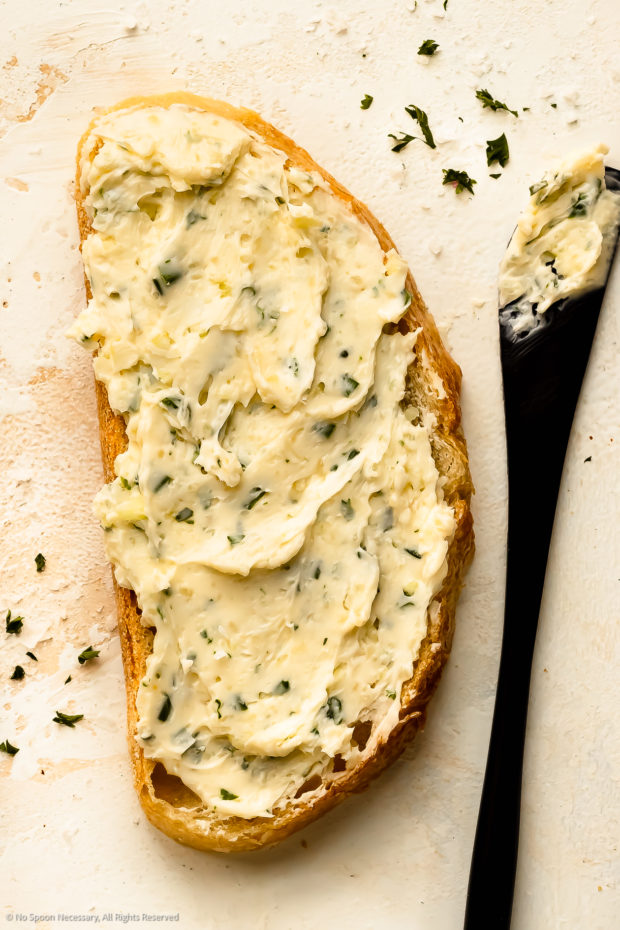 Overhead photo of homemade garlic butter spread on a slice of bread with a butter spreading knife next to the piece of toast.