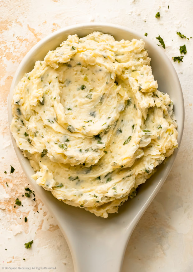 Overhead photo of soft garlic butter with herbs in a white butter serving dish.
