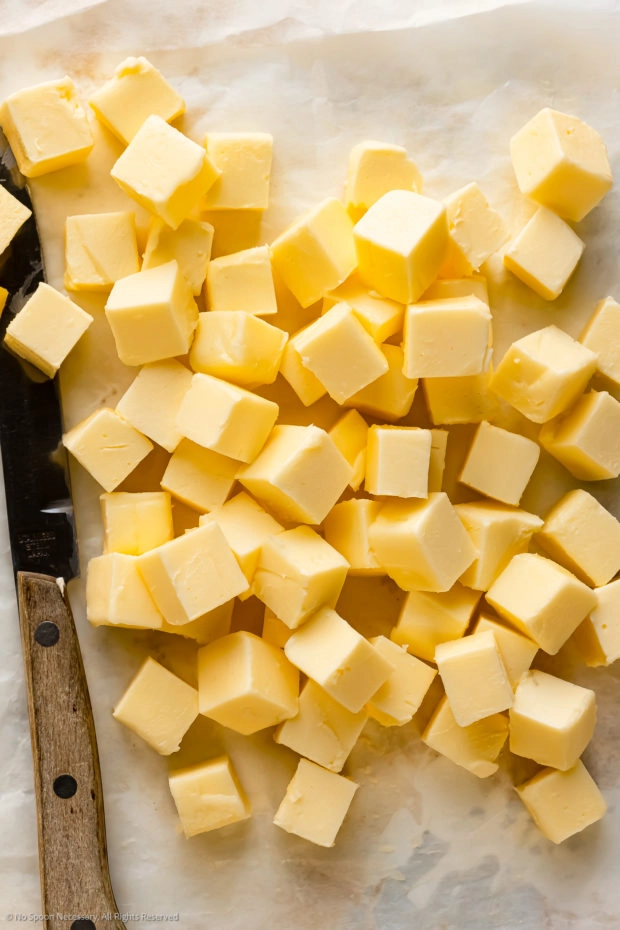 Overhead photo of softened, cubes of butter on a piece of parchment paper.