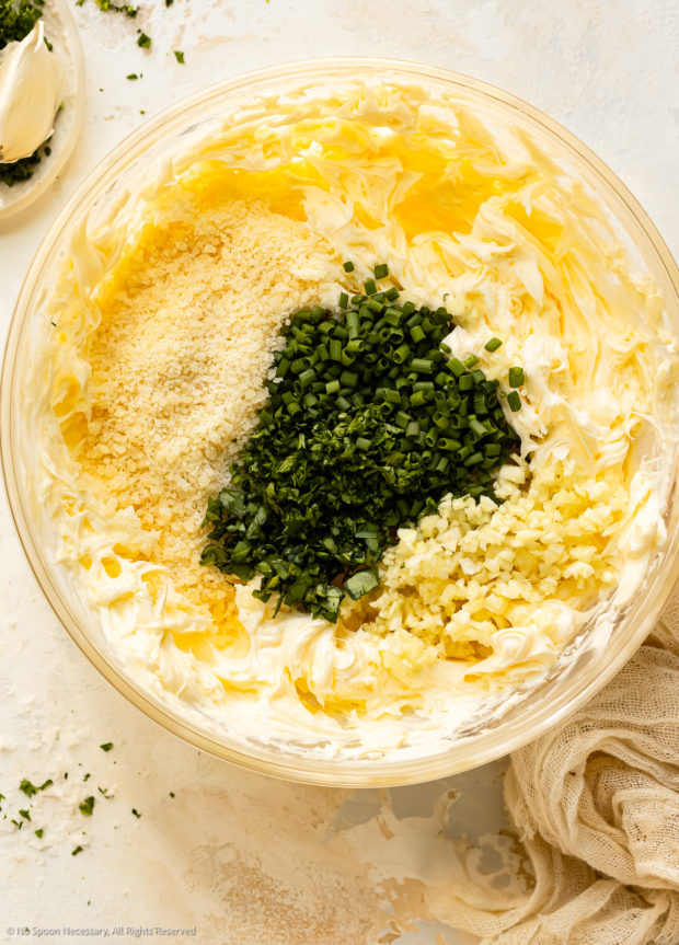 Overhead photo of all the ingredients to make herb garlic spread in a medium mixing bowl.