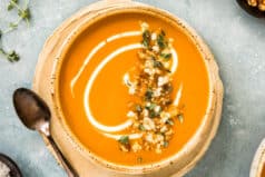 Overhead photo of Sweet Potatoes Soup topped with fresh herbs and creme fraiche in a soup bowl.