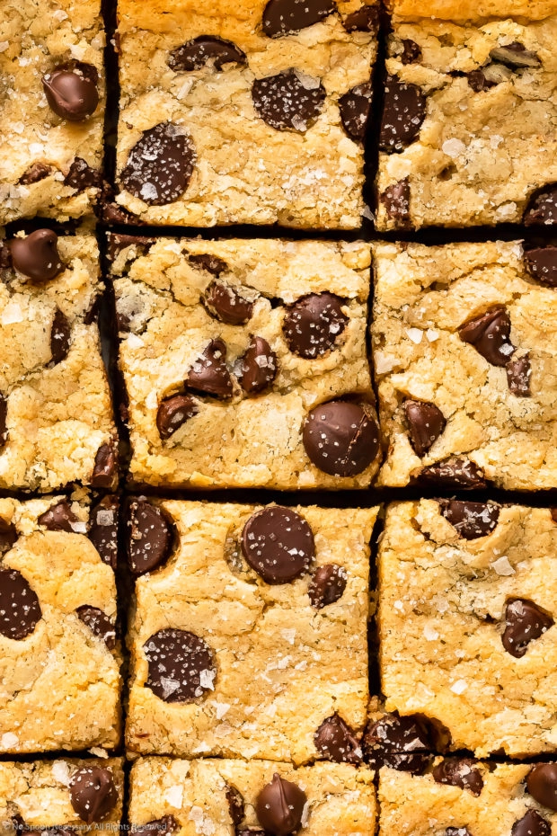 Close-up overhead photo of cookie bars studded with chocolate chips and dusted with flakey sea salt.