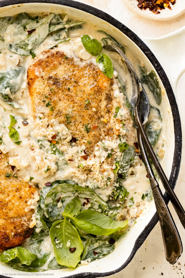 Overhead photo of cooked chicken breasts and spinach in creamy white sauce.