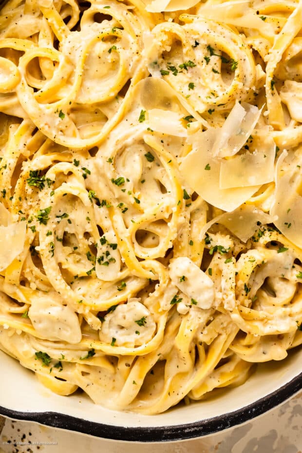 Overhead photo of cream cheese sauce pasta garnished with fresh parsley and shaved parmesan cheese in a white skillet.