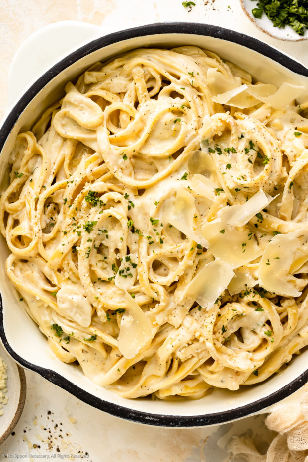 Overhead photo of creamy cheese pasta with fresh parmesan in a large white skillet.