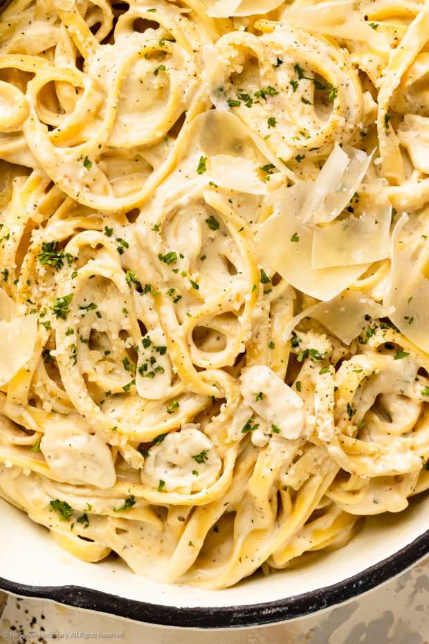 Overhead, close-up photo of fettuccine noodles with cream cheese sauce, grated parmesan and fresh parsley. 