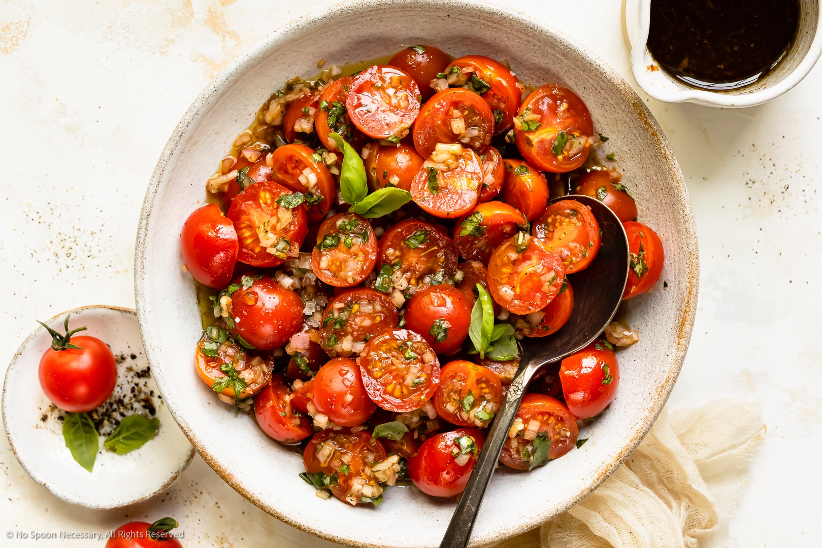 Overhead photo of marinated tomatoes with garlic and basil in a serving bowl with a serving spoon.
