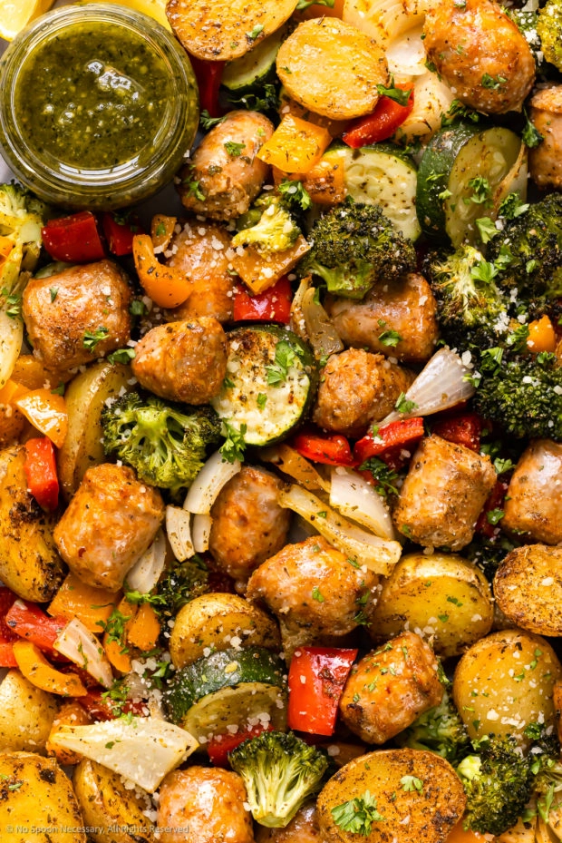 Overhead, close-up photo of roasted sausage and veggies, including broccoli, zucchini and bell peppers.