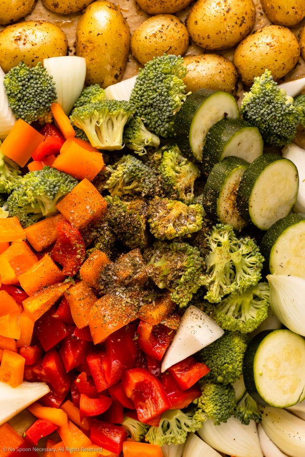 Overhead photo of a pile of fresh vegetables (broccoli, onions, bell peppers, zucchini and petite potatoes) topped with Italian seasonings. 