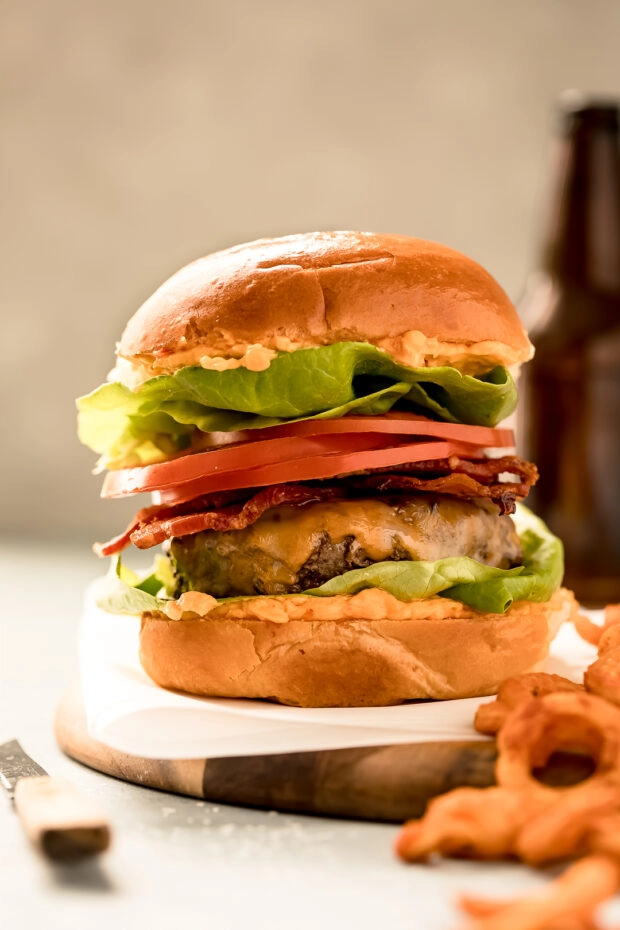 Straight on photo of a bacon cheeseburger made with hamburger spices, lettuce, and tomatoes.
