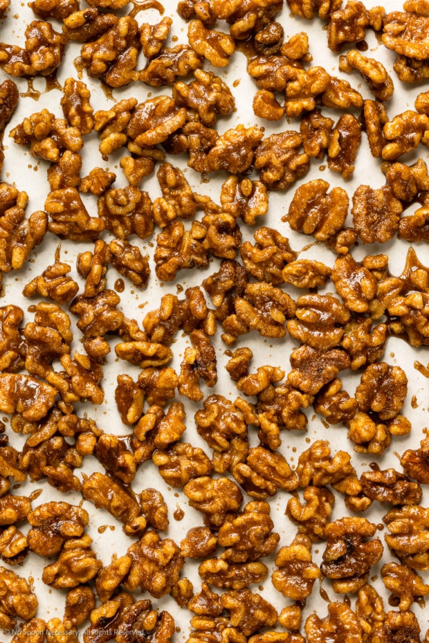 Overhead photo of maple candied walnuts spread out on a parchment-lined baking pan.
