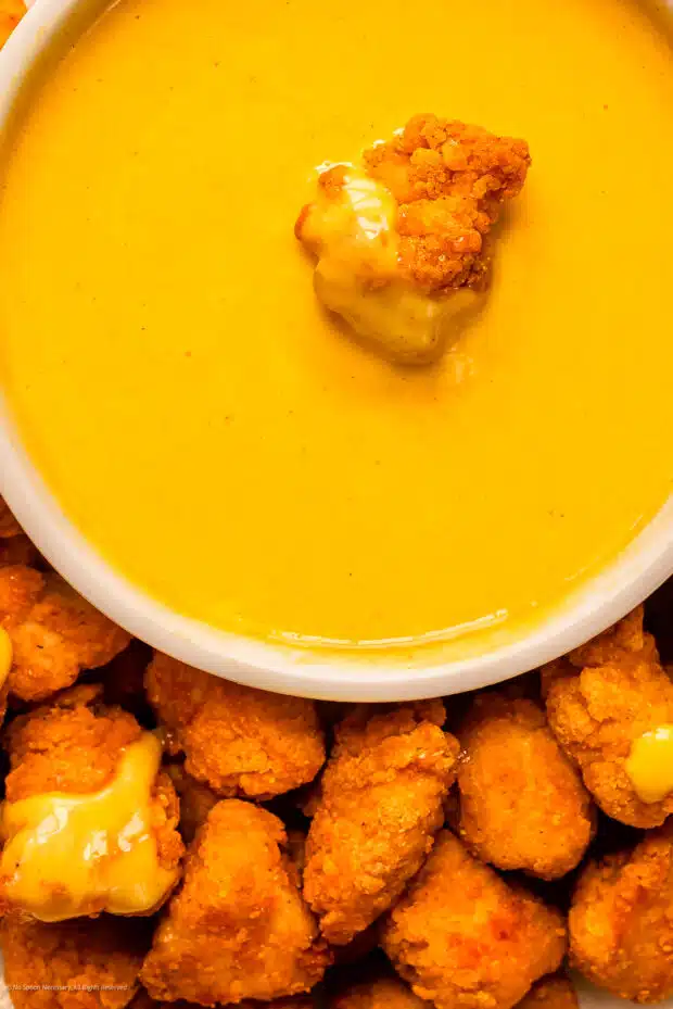 Close-up photo of a chicken nugget dipped into a homemade mustard sauce.