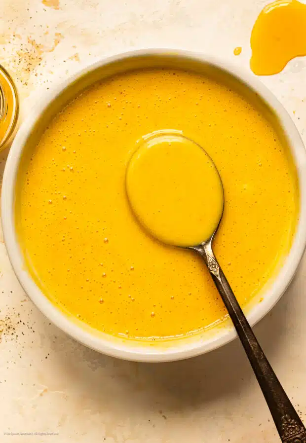Overhead photo of a spoon dipped into a yellow mustard sauce.