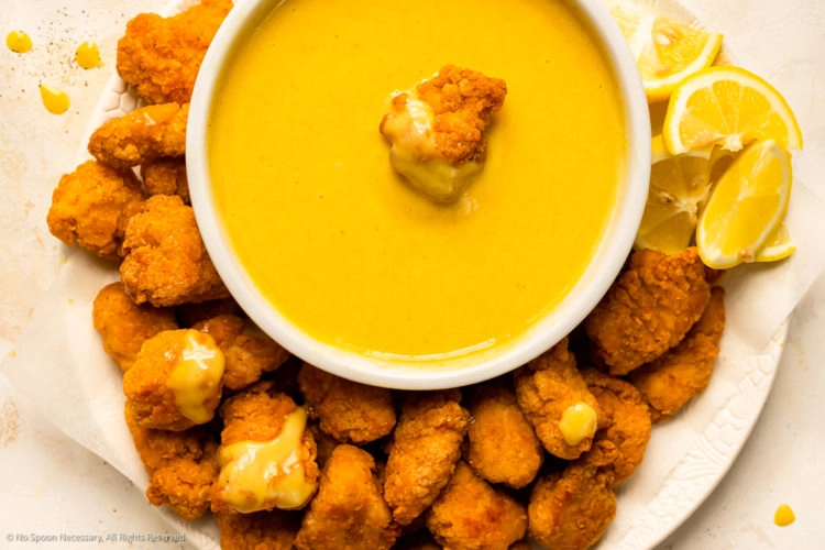 Overhead photo of honey mustard sauce in a white bowl with a chicken nugget resting in the sauce.