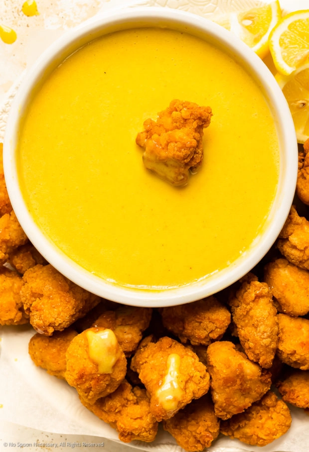 Overhead photo of honey mustard in a white bowl with a pile of chicken nuggets next to the sauce bowl.