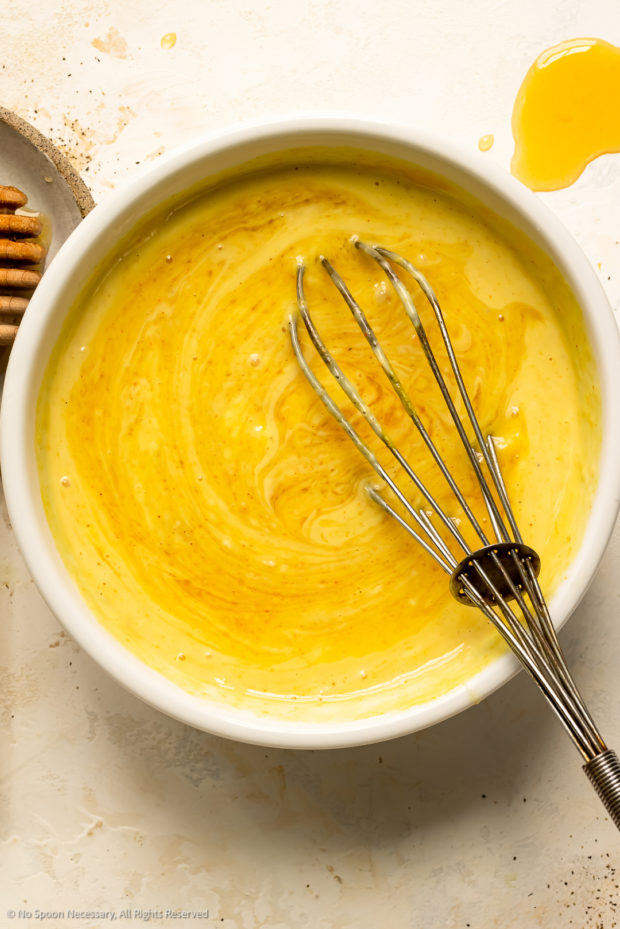 Overhead photo of a whisk combining honey mustard dip ingredients in a white bowl.