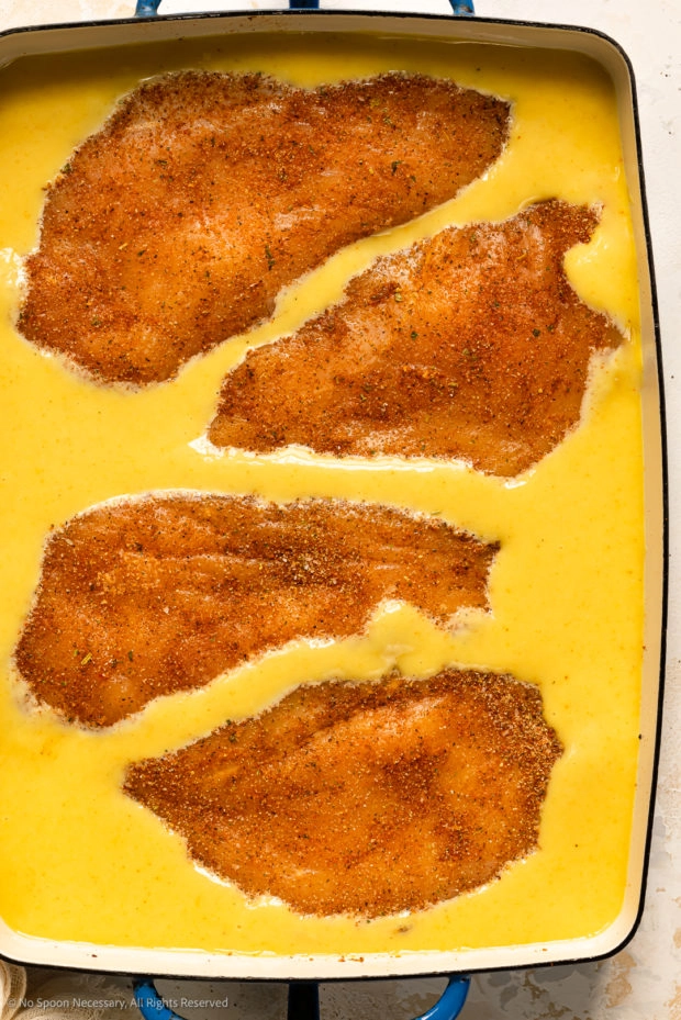 Overhead photo of a baking dish with four seasoned chicken breasts in honey mustard sauce.