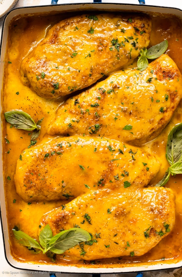 Overhead photo of mustard chicken breasts garnished with fresh basil in a baking pan. 