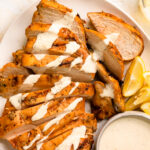Overhead photo of a platter of smoked chicken breasts sliced and drizzled with Alabama white sauce.