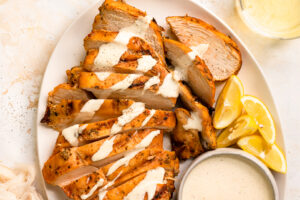 Overhead photo of a platter of smoked chicken breasts sliced and drizzled with Alabama white sauce.