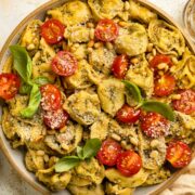 Overhead photo of a bowl of pesto tortellini with cherry tomatoes, parmesan cheese and basil.