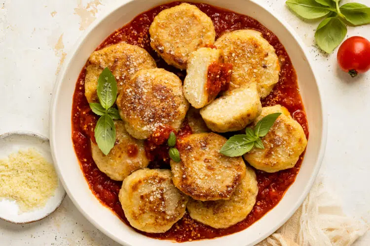 Overhead photo of ricotta gnocchi with basil and marinara in a white bowl.