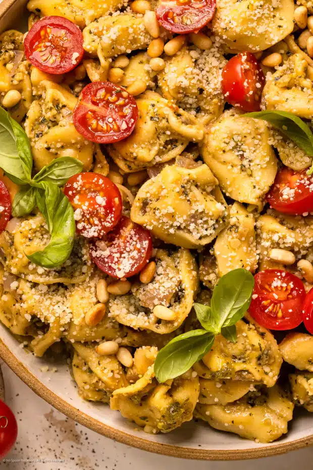 Overhead, close up photo of tortellini in pesto sauce with tomatoes, parmesan, and basil.