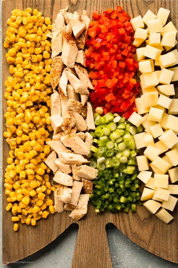 Overhead photo of diced potatoes, chopped cooked chicken, corn kernels, chopped peppers, and herbs on a wood cutting board.