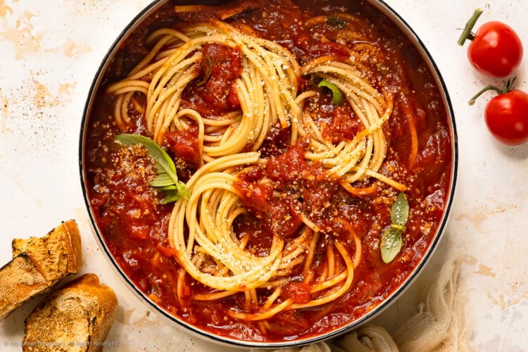 Overhead photo of spaghetti marinara with fresh basil leaves in a large white pot.